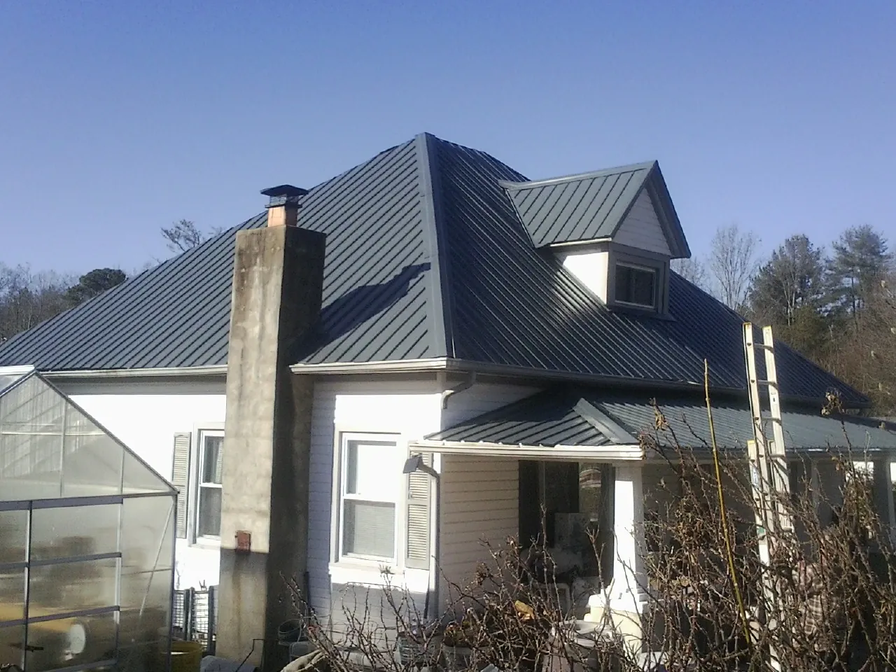 Dark blue standing seam metal roof on a white farmhouse with dormer — Slate & Tile Roof Repair by Roofing Brothers in Latta