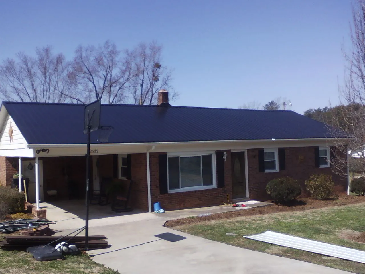 Finished dark blue metal roof on a brick ranch with a carport in Latta