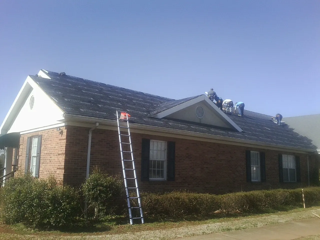 Crew tearing shingles off a brick ranch roof with a ladder set — Emergency Roof Repair work by our crew in Latta