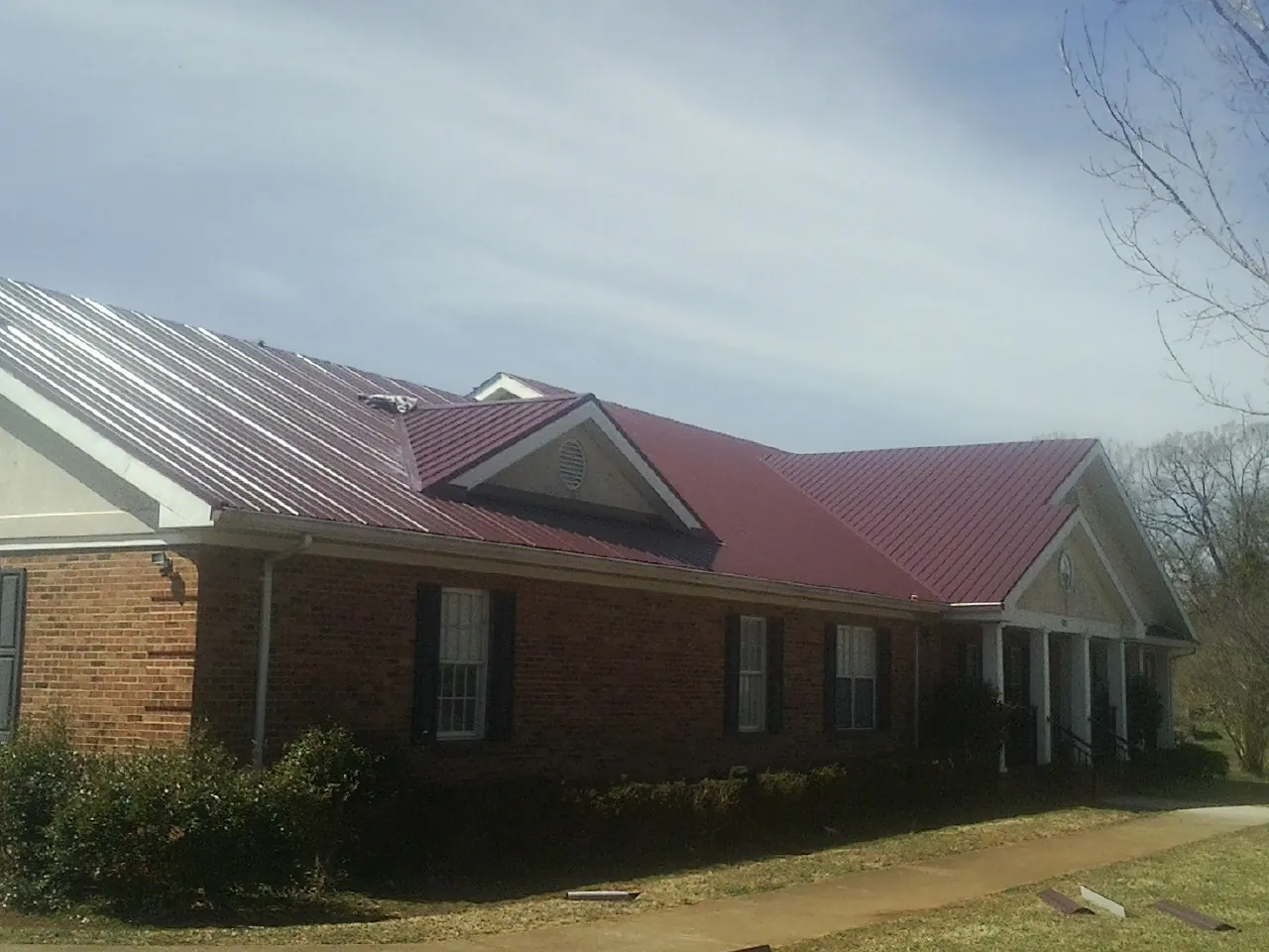 Red metal roof with gabled entries on a long brick building, from a Hail Damage Roof Repair job in Latta