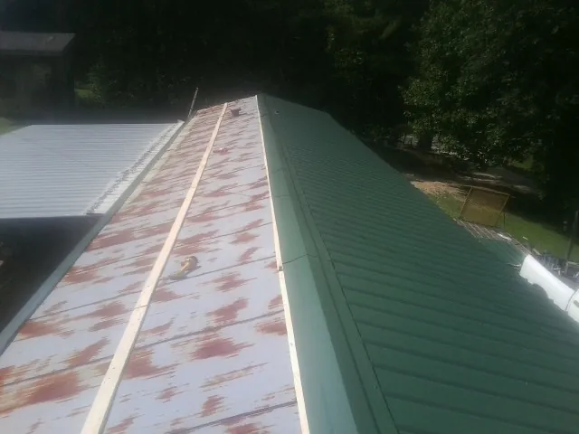 Old rusted panels beside newly installed green metal roofing — Wind Damage Roof Repair by Roofing Brothers in Latta