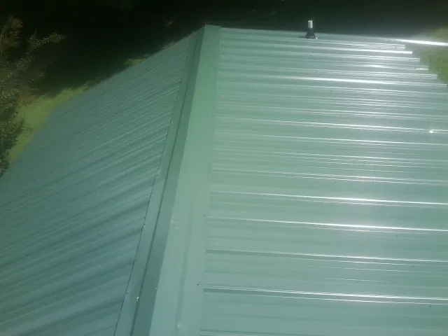 New green metal panels meeting at the ridge of a roof — Flat Roof Repair work by our crew in Latta