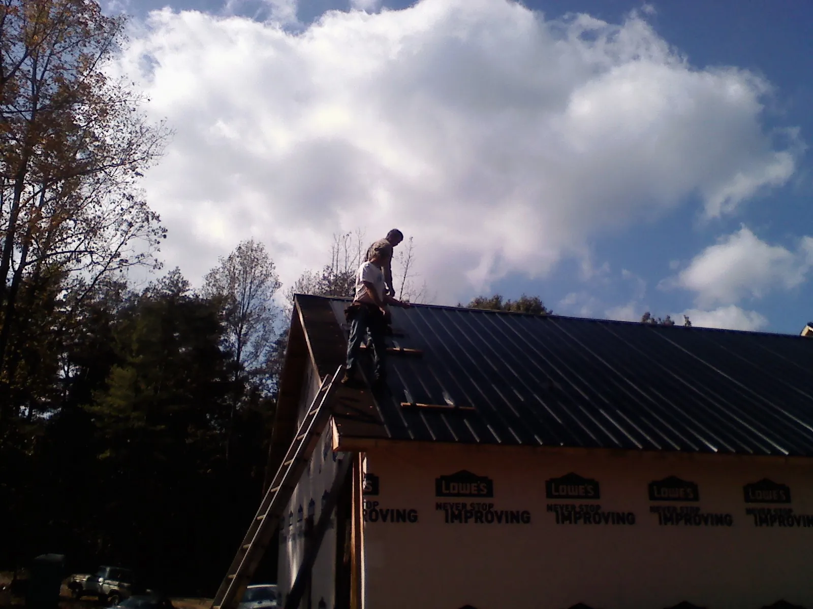 Roofer fastening dark metal panels high against a cloudy sky, from a Roof Inspection job in Latta