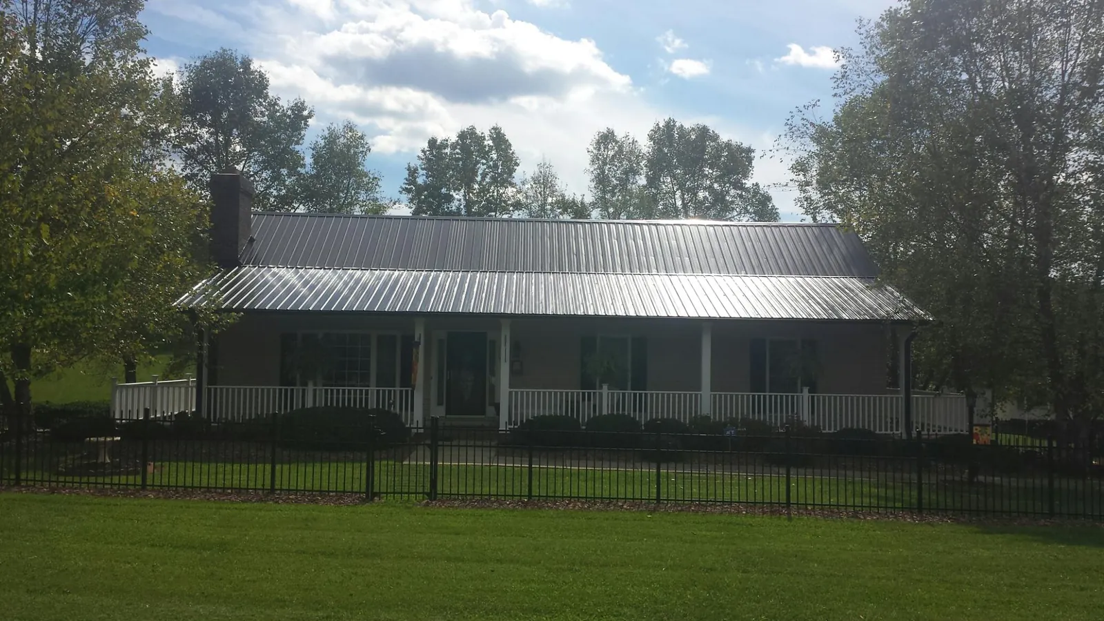 Gray metal roof on a brick ranch with a full width front porch — Gutter Guard Installation work by our crew in Latta