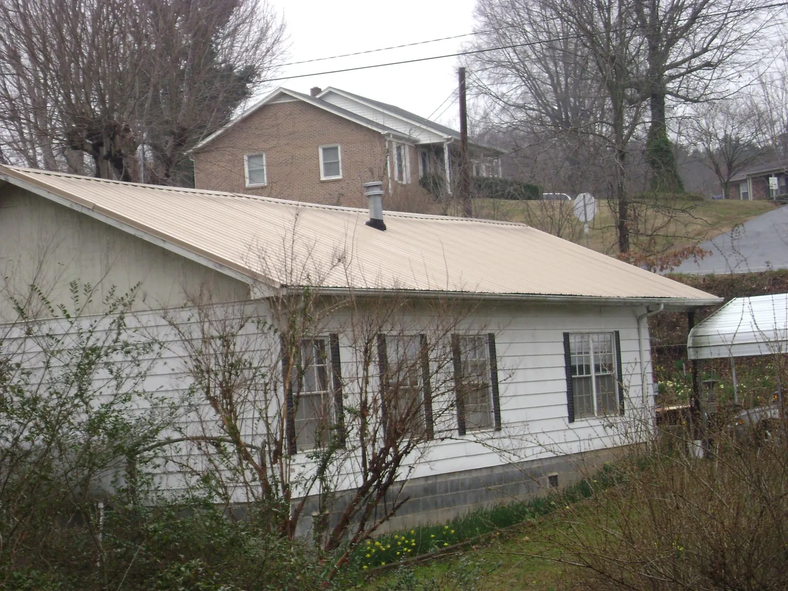 Tan metal roof on a white sided house set into a hillside — Commercial Roofing by Roofing Brothers in Latta