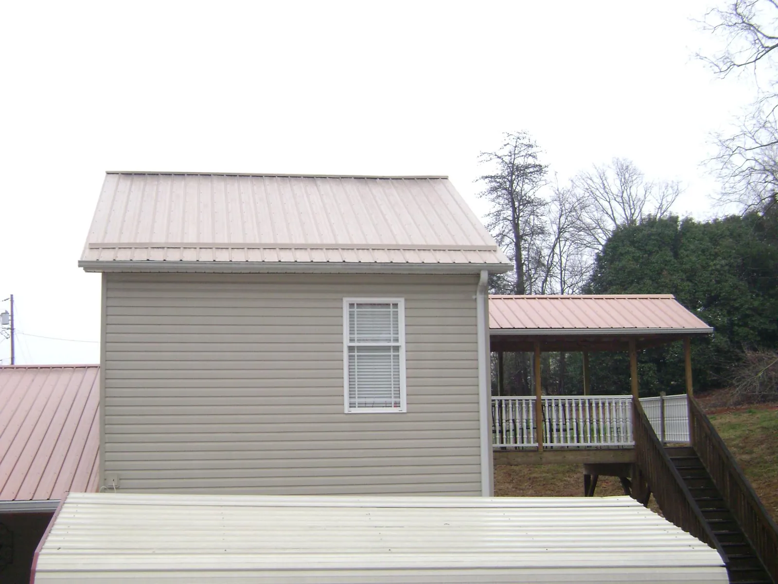 Tan metal roofs on a two story addition and attached porch, from a Roof Replacement job in Latta